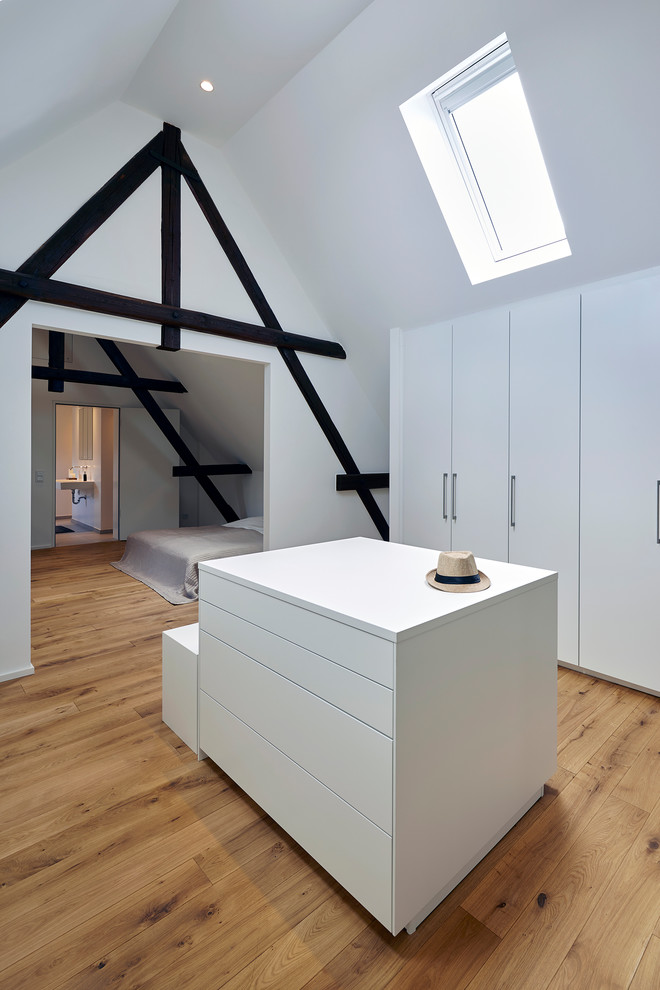 This is an example of a large contemporary gender-neutral walk-in wardrobe in Cologne with flat-panel cabinets, white cabinets, medium hardwood floors and brown floor.