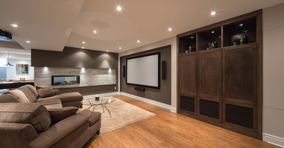 This is an example of a large contemporary fully buried basement in Ottawa with laminate floors, a two-sided fireplace, a tile fireplace surround, beige walls and brown floor.