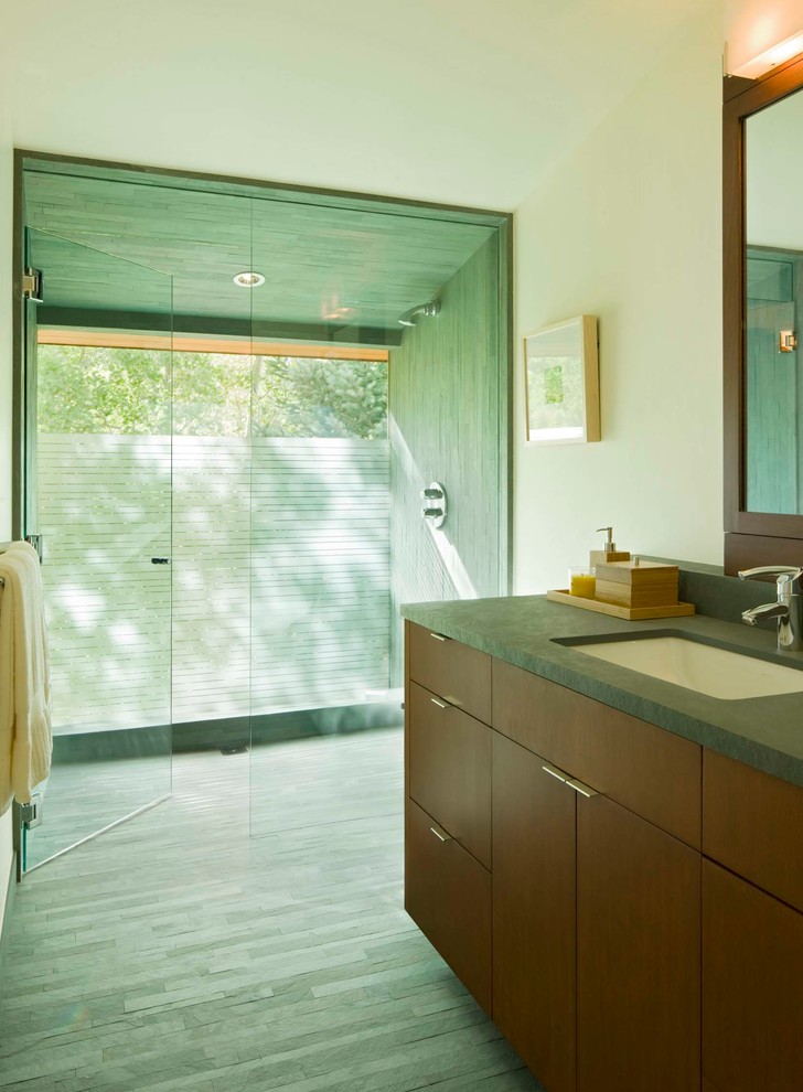 Photo of a large modern master bathroom in Denver with flat-panel cabinets, dark wood cabinets, a curbless shower, a wall-mount toilet, green tile, slate, white walls, slate floors, an undermount sink, soapstone benchtops, green floor and a hinged shower door.
