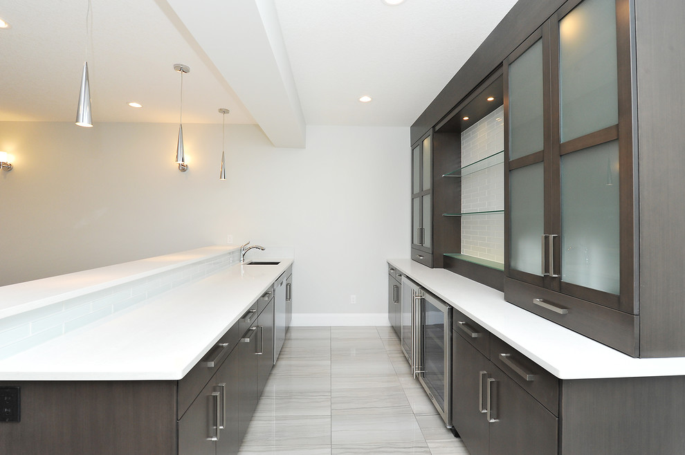 This is an example of a mid-sized modern galley wet bar in Calgary with an undermount sink, flat-panel cabinets, dark wood cabinets, solid surface benchtops, porcelain floors, grey floor and white benchtop.