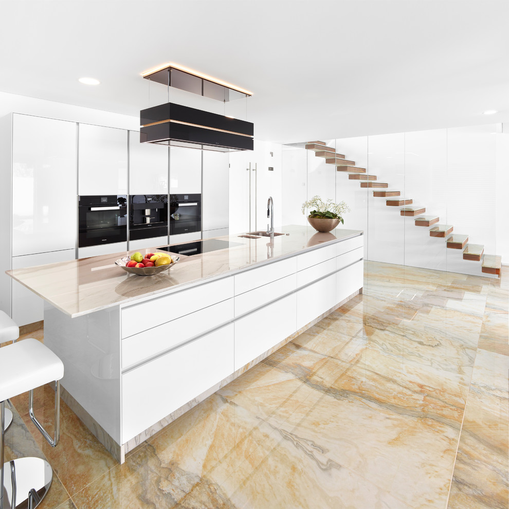 Inspiration for a contemporary galley open plan kitchen in Other with flat-panel cabinets, black appliances, marble floors, with island, beige floor, an undermount sink and quartzite benchtops.