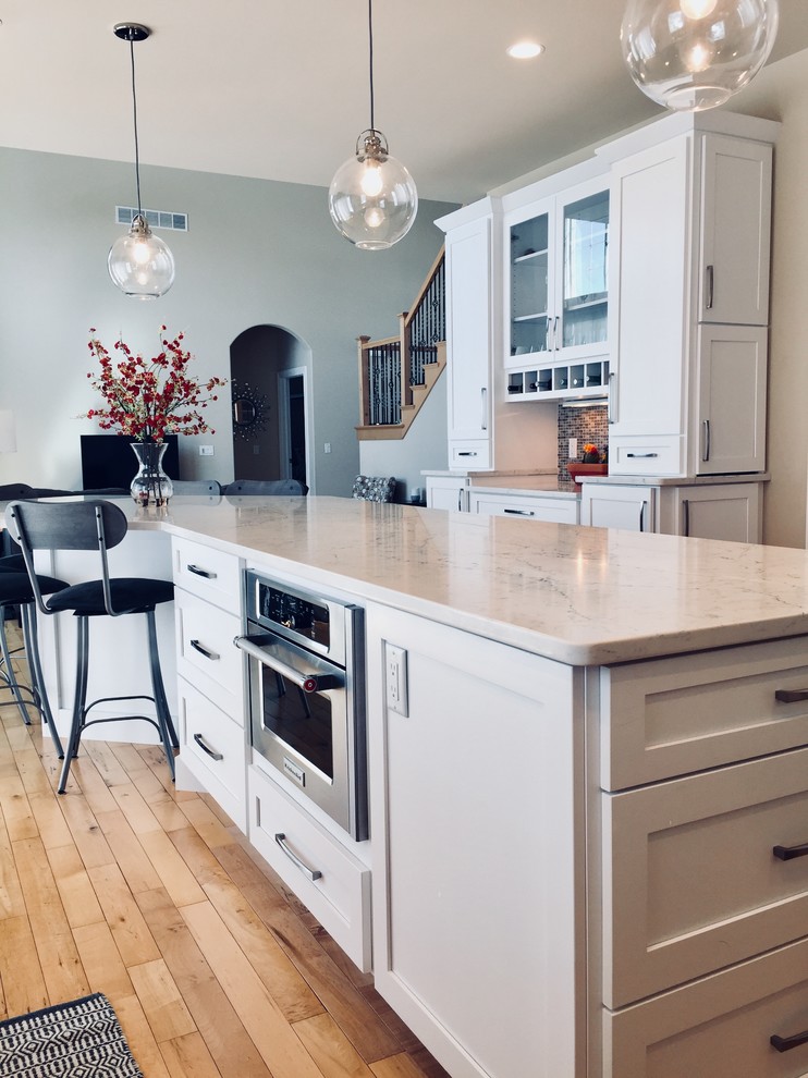 Kitchen - mid-sized transitional light wood floor kitchen idea with an undermount sink, shaker cabinets, white cabinets, quartz countertops, blue backsplash, glass tile backsplash, stainless steel appliances and an island