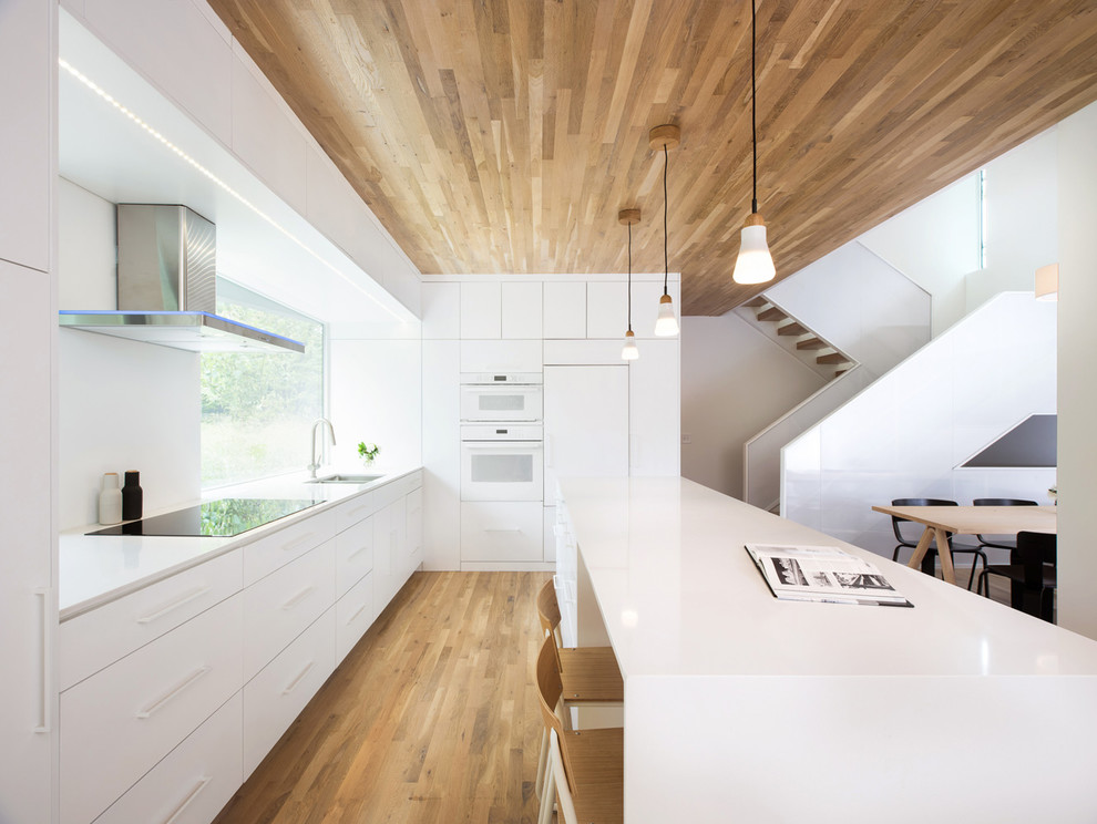 Inspiration for a modern l-shaped eat-in kitchen in Minneapolis with flat-panel cabinets, white cabinets, white appliances, medium hardwood floors, with island and brown floor.
