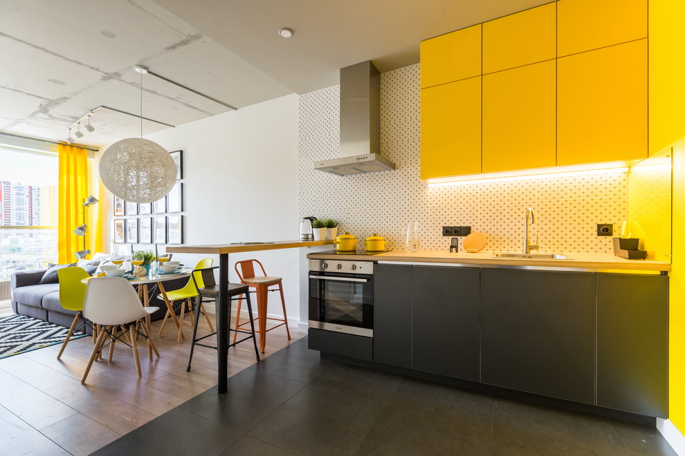 Inspiration for a contemporary l-shaped open plan kitchen in Saint Petersburg with a drop-in sink, flat-panel cabinets, yellow cabinets, wood benchtops, white splashback, stainless steel appliances, no island, black floor and beige benchtop.