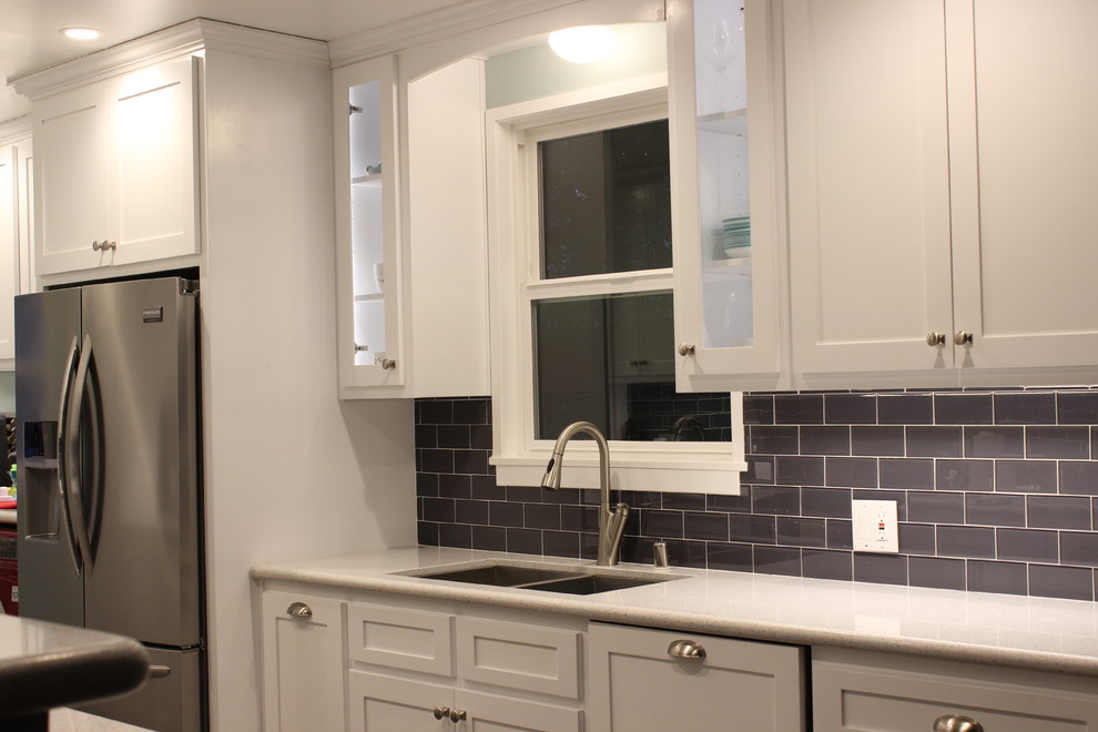 This is an example of a transitional galley eat-in kitchen in Los Angeles with an undermount sink, shaker cabinets, white cabinets, quartz benchtops, grey splashback, glass tile splashback and stainless steel appliances.