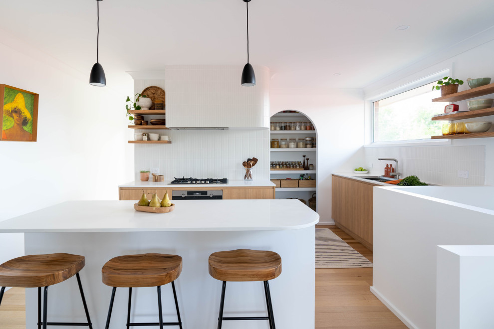 This is an example of a scandinavian l-shaped kitchen in Canberra - Queanbeyan with an undermount sink, flat-panel cabinets, medium wood cabinets, white splashback, stainless steel appliances, medium hardwood floors, with island, brown floor and white benchtop.