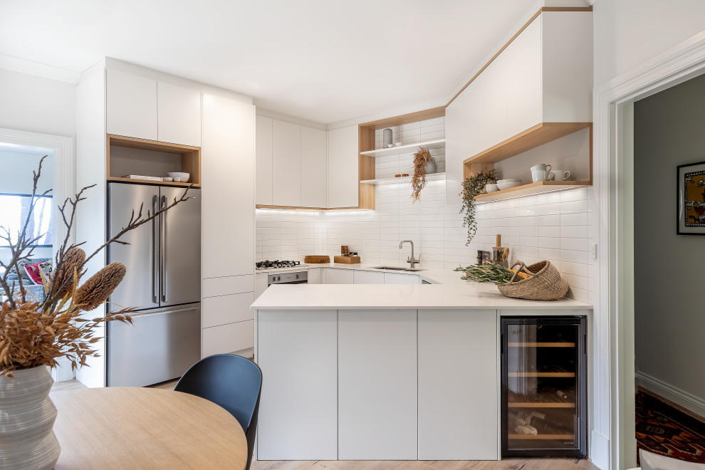 Example of a small trendy u-shaped laminate floor and brown floor eat-in kitchen design in Adelaide with an undermount sink, flat-panel cabinets, white cabinets, quartz countertops, white backsplash, subway tile backsplash, stainless steel appliances, a peninsula and white countertops