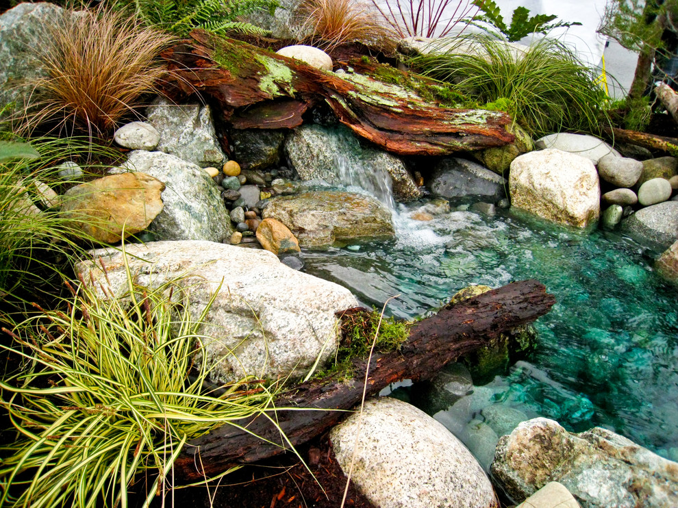 This is an example of a mid-sized rustic full sun backyard stone water fountain landscape in Seattle for spring.
