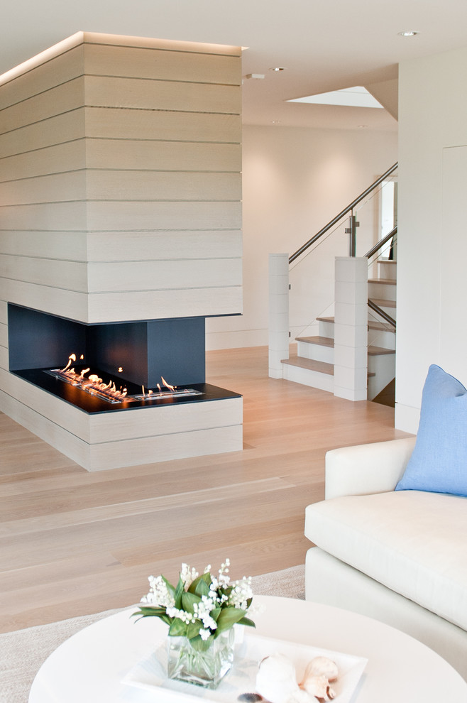 This is an example of a beach style living room in Boston with light hardwood floors and a two-sided fireplace.