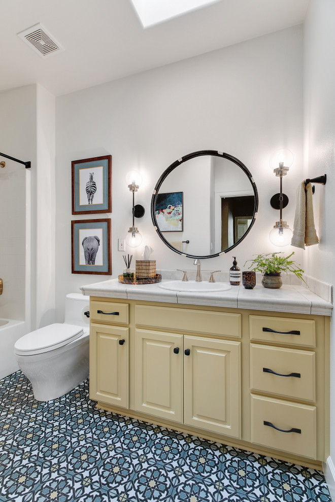 Example of a mid-sized eclectic 3/4 multicolored tile and ceramic tile porcelain tile, multicolored floor, single-sink and vaulted ceiling bathroom design in Portland with raised-panel cabinets, yellow cabinets, a one-piece toilet, white walls, a drop-in sink, tile countertops, beige countertops and a built-in vanity