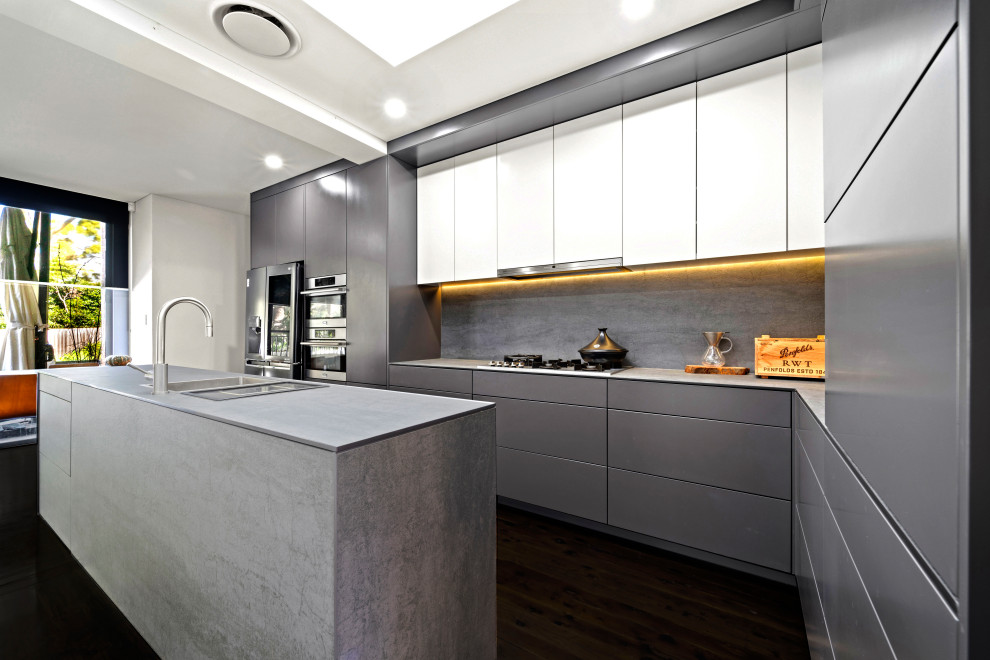 Inspiration for a mid-sized contemporary l-shaped kitchen in Sydney with a double-bowl sink, flat-panel cabinets, grey cabinets, grey splashback, porcelain splashback, stainless steel appliances, painted wood floors, with island, black floor and grey benchtop.