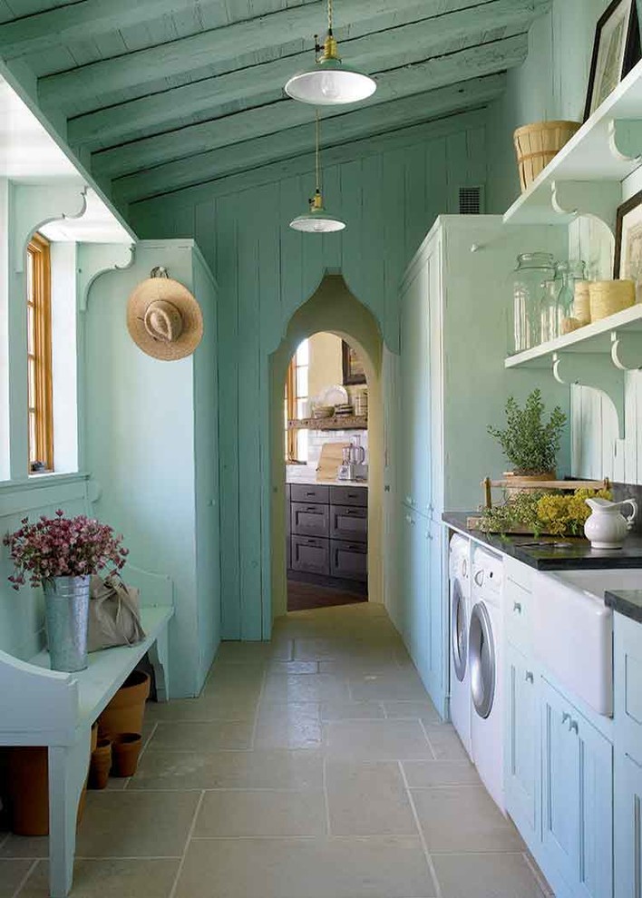 Design ideas for a mediterranean galley dedicated laundry room in Austin with a farmhouse sink, recessed-panel cabinets, blue cabinets, blue walls, a side-by-side washer and dryer and grey floor.
