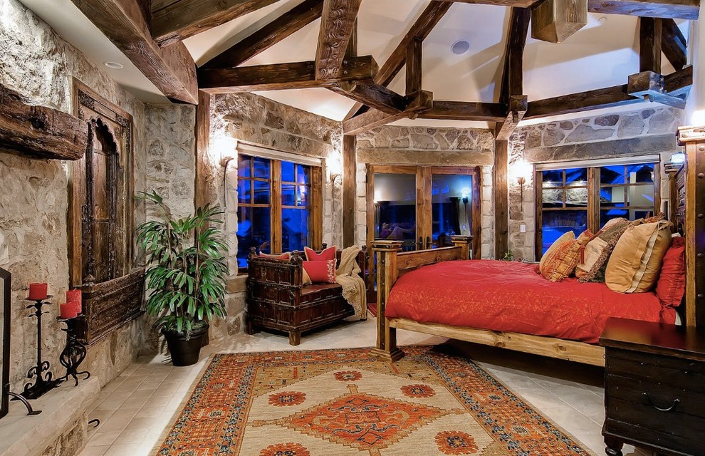 Photo of a large country guest bedroom in Denver with brown walls, travertine floors, a standard fireplace, a stone fireplace surround and beige floor.