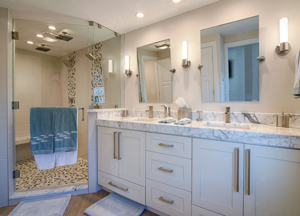 Design ideas for a mid-sized contemporary master bathroom in Miami with white cabinets, a corner shower, a two-piece toilet, white walls, light hardwood floors, an undermount sink, brown floor, a hinged shower door, shaker cabinets, beige tile, pebble tile and marble benchtops.
