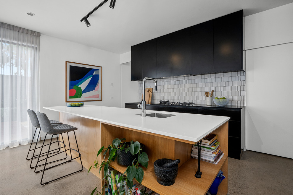 This is an example of a contemporary open plan kitchen in Geelong with a drop-in sink, black cabinets, quartz benchtops, white splashback, porcelain splashback, concrete floors, with island, grey floor and multi-coloured benchtop.