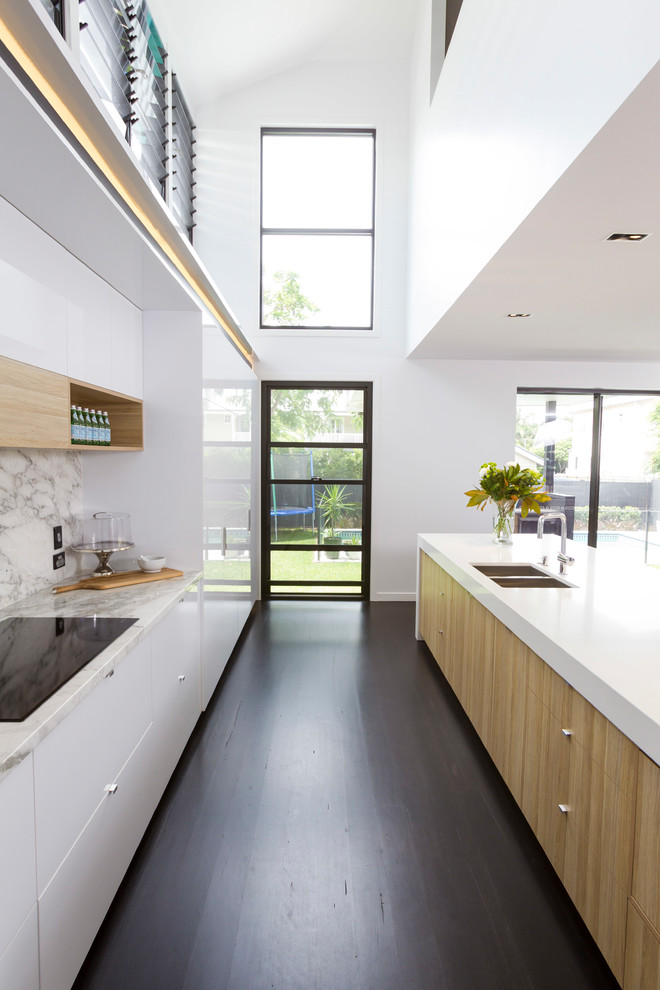 This is an example of a large contemporary galley kitchen in Brisbane with dark hardwood floors, with island, flat-panel cabinets, white cabinets, grey splashback, brown floor and white benchtop.