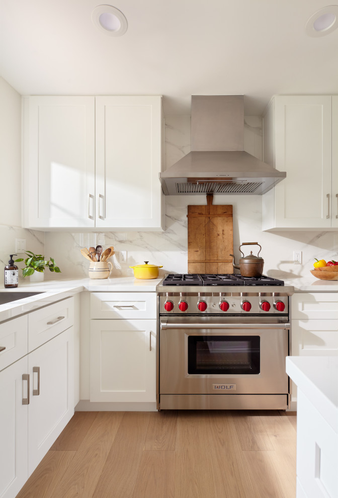 Inspiration for a mid-sized transitional l-shaped light wood floor and brown floor eat-in kitchen remodel with an undermount sink, shaker cabinets, white cabinets, quartz countertops, white backsplash, porcelain backsplash, stainless steel appliances, an island and white countertops