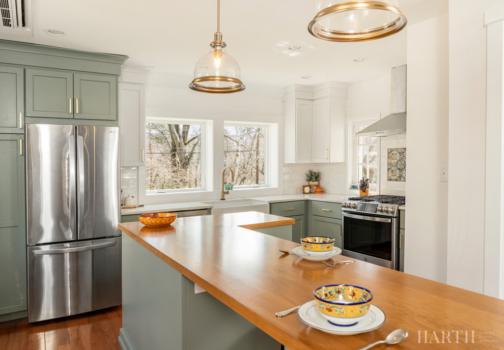 Inspiration for a mid-sized cottage l-shaped medium tone wood floor and brown floor enclosed kitchen remodel in Philadelphia with a farmhouse sink, shaker cabinets, green cabinets, quartz countertops, white backsplash, subway tile backsplash, stainless steel appliances, an island and white countertops