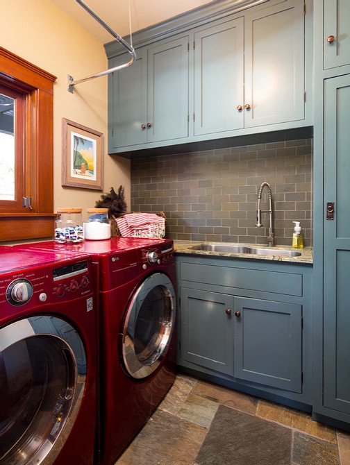 Exempel på en mellanstor amerikansk l-formad tvättstuga enbart för tvätt, med en undermonterad diskho, skåp i shakerstil, blå skåp, marmorbänkskiva, grönt stänkskydd, stänkskydd i tunnelbanekakel, beige väggar, skiffergolv, en tvättmaskin och torktumlare bredvid varandra och flerfärgat golv