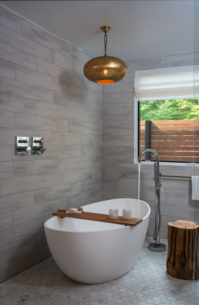 Contemporary master bathroom in New York with a freestanding tub, gray tile, grey walls and grey floor.
