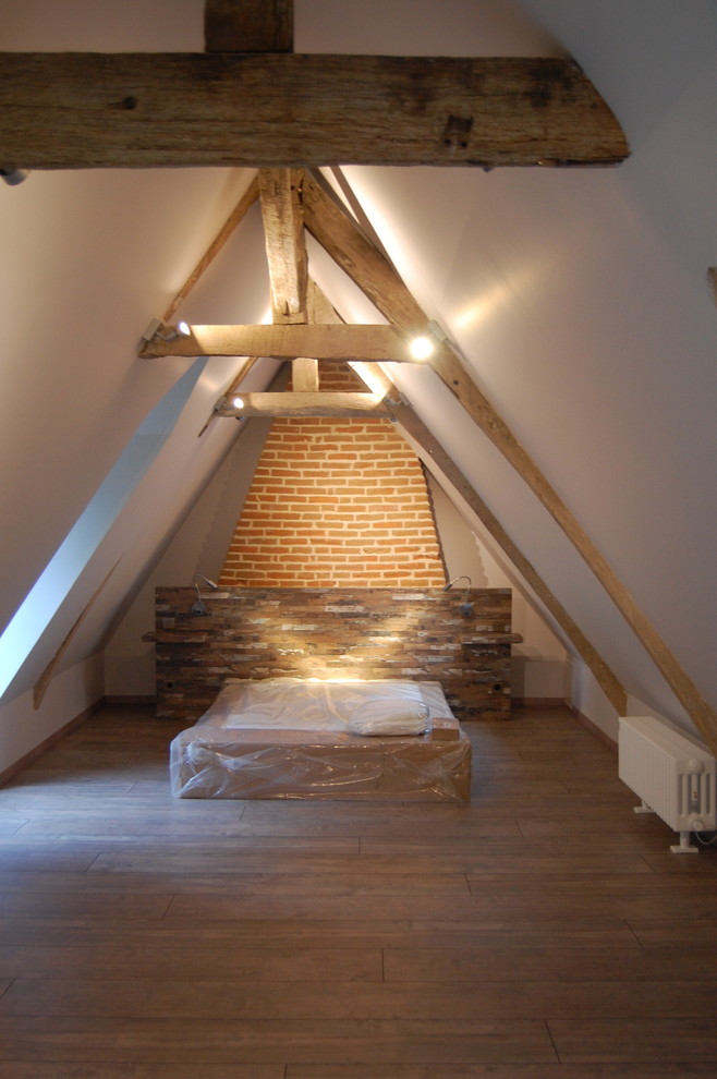 Large country loft-style bedroom in Paris with white walls, dark hardwood floors, no fireplace and brown floor.