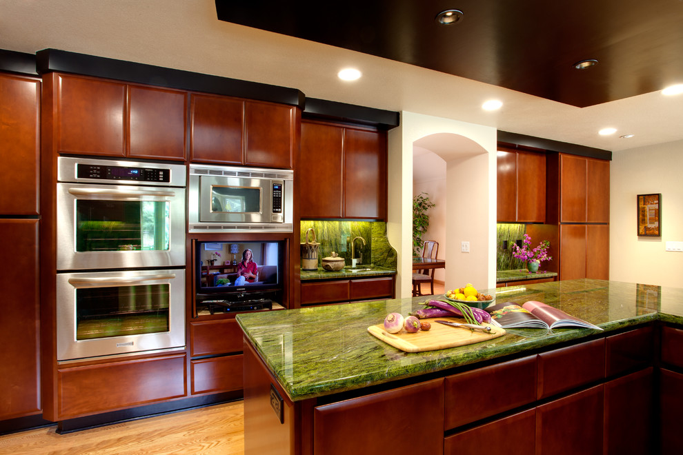 This is an example of an asian kitchen in San Francisco with flat-panel cabinets, medium wood cabinets, granite benchtops, green splashback, stone slab splashback, stainless steel appliances and light hardwood floors.