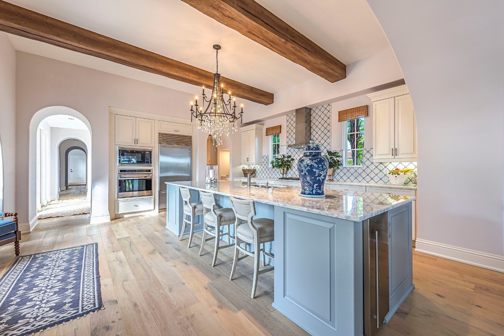 Inspiration for a beach style l-shaped kitchen in New Orleans with an undermount sink, raised-panel cabinets, blue cabinets, white splashback, stainless steel appliances, medium hardwood floors, with island and brown floor.