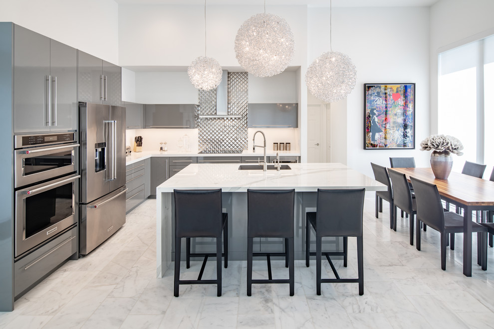 Large contemporary l-shaped open plan kitchen in Miami with an undermount sink, flat-panel cabinets, grey cabinets, quartz benchtops, white splashback, metal splashback, stainless steel appliances, marble floors, with island, white floor and white benchtop.