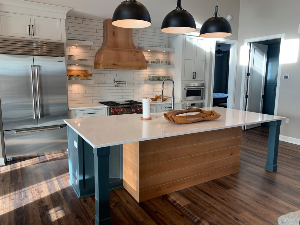 Large mountain style single-wall vinyl floor and brown floor eat-in kitchen photo with shaker cabinets, white cabinets, quartz countertops, white backsplash, subway tile backsplash, stainless steel appliances, an island and white countertops
