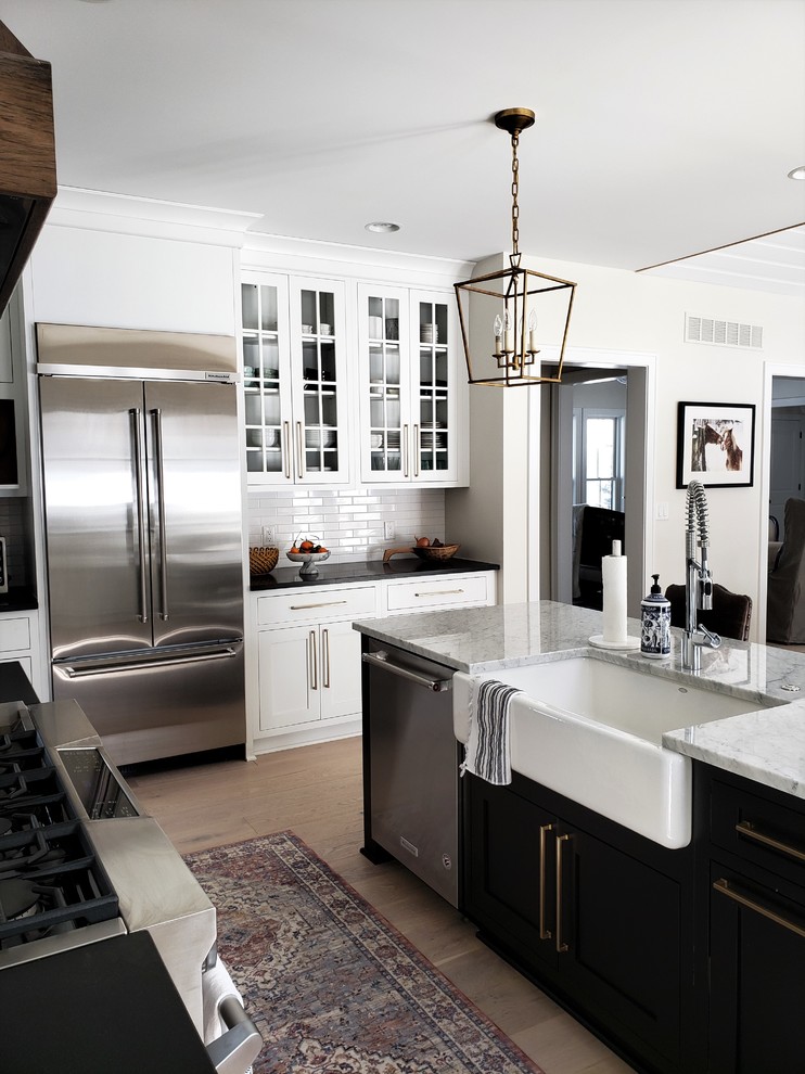 Photo of a mid-sized country u-shaped eat-in kitchen in Detroit with a farmhouse sink, recessed-panel cabinets, white cabinets, quartz benchtops, white splashback, subway tile splashback, stainless steel appliances, light hardwood floors, with island, beige floor and white benchtop.