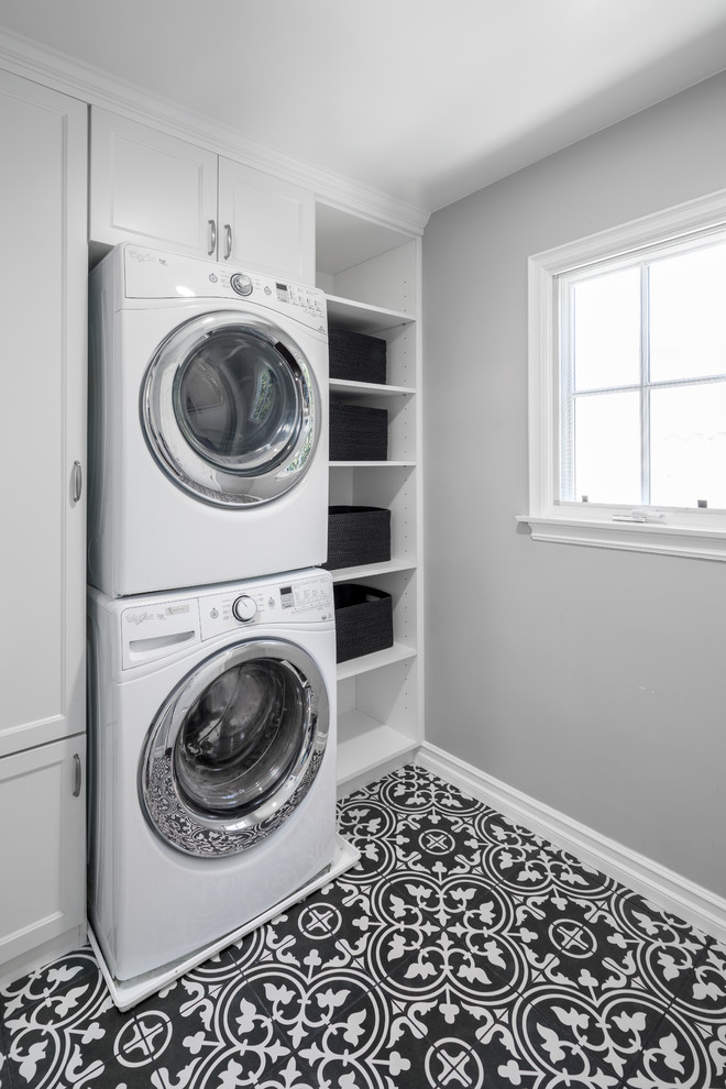 Design ideas for a small transitional single-wall dedicated laundry room in Los Angeles with beaded inset cabinets, white cabinets, grey walls, porcelain floors, a stacked washer and dryer and black floor.