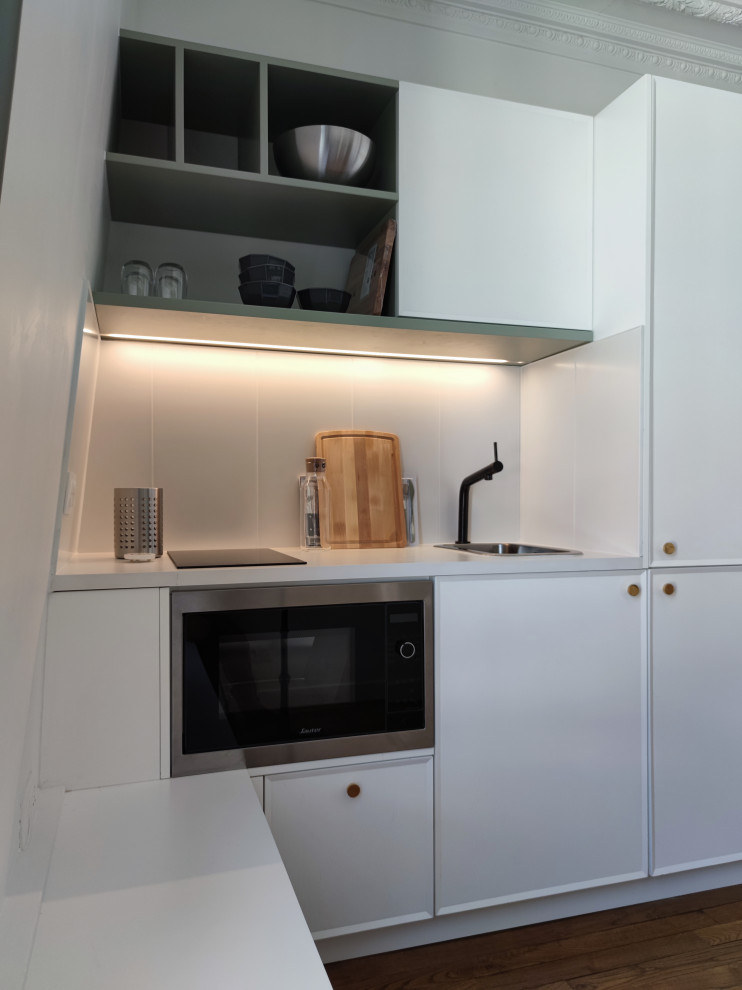 Bild på ett litet vit linjärt vitt kök, med en undermonterad diskho, luckor med profilerade fronter, vita skåp, bänkskiva i kvartsit, vitt stänkskydd, stänkskydd i keramik, rostfria vitvaror, ljust trägolv och brunt golv