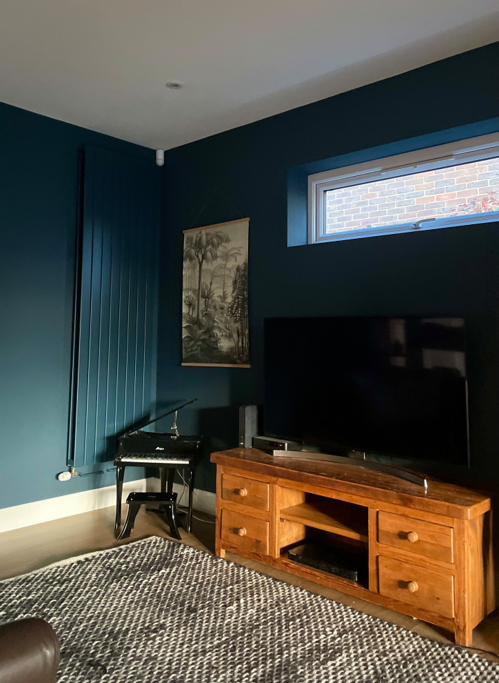 Small contemporary enclosed living room in Hertfordshire with blue walls, light hardwood floors, no fireplace, a freestanding tv and brown floor.
