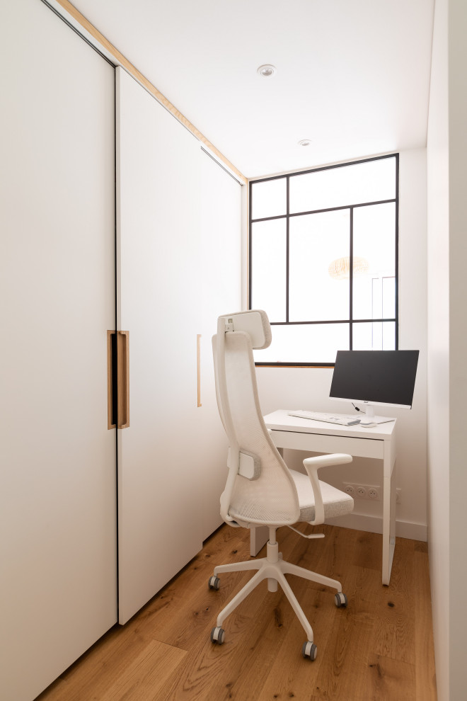 Immagine di uno studio moderno di medie dimensioni con pareti bianche, parquet chiaro e scrivania autoportante