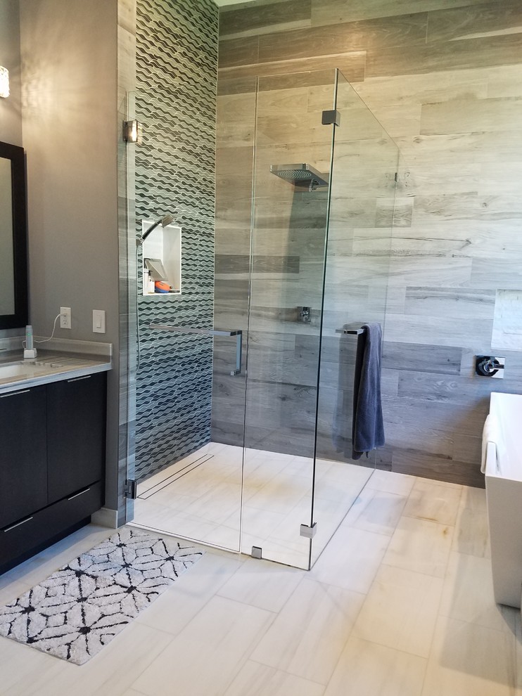 This is an example of a mid-sized transitional master bathroom in Miami with flat-panel cabinets, black cabinets, a freestanding tub, a corner shower, a one-piece toilet, gray tile, porcelain tile, grey walls, marble floors, an undermount sink, marble benchtops, white floor and a hinged shower door.