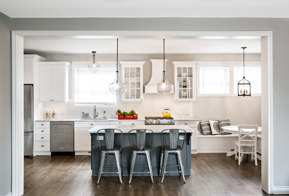 Photo of a large transitional single-wall eat-in kitchen in Detroit with a drop-in sink, shaker cabinets, white cabinets, white splashback, subway tile splashback, stainless steel appliances, dark hardwood floors and with island.
