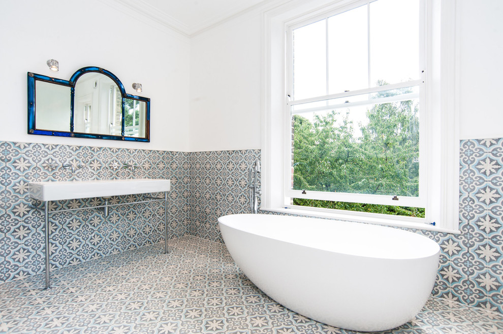 Transitional bathroom in London with a freestanding tub, multi-coloured tile, white walls, ceramic floors and a console sink.
