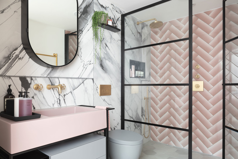 Inspiration for a mid-sized modern master bathroom in London with furniture-like cabinets, an open shower, a wall-mount toilet, pink tile, subway tile, pink walls, cement tiles, solid surface benchtops, grey floor, a hinged shower door and pink benchtops.