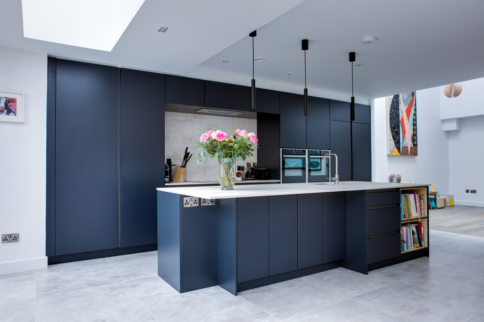 This is an example of a mid-sized contemporary galley open plan kitchen in Dublin with a drop-in sink, flat-panel cabinets, blue cabinets, quartzite benchtops, grey splashback, stone slab splashback, stainless steel appliances, porcelain floors, with island, grey floor and grey benchtop.