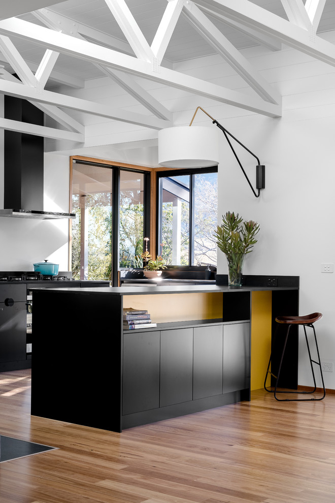 Inspiration for a large midcentury u-shaped eat-in kitchen in Other with flat-panel cabinets, black cabinets, solid surface benchtops, window splashback, stainless steel appliances, medium hardwood floors, a peninsula, black benchtop, white splashback and brown floor.