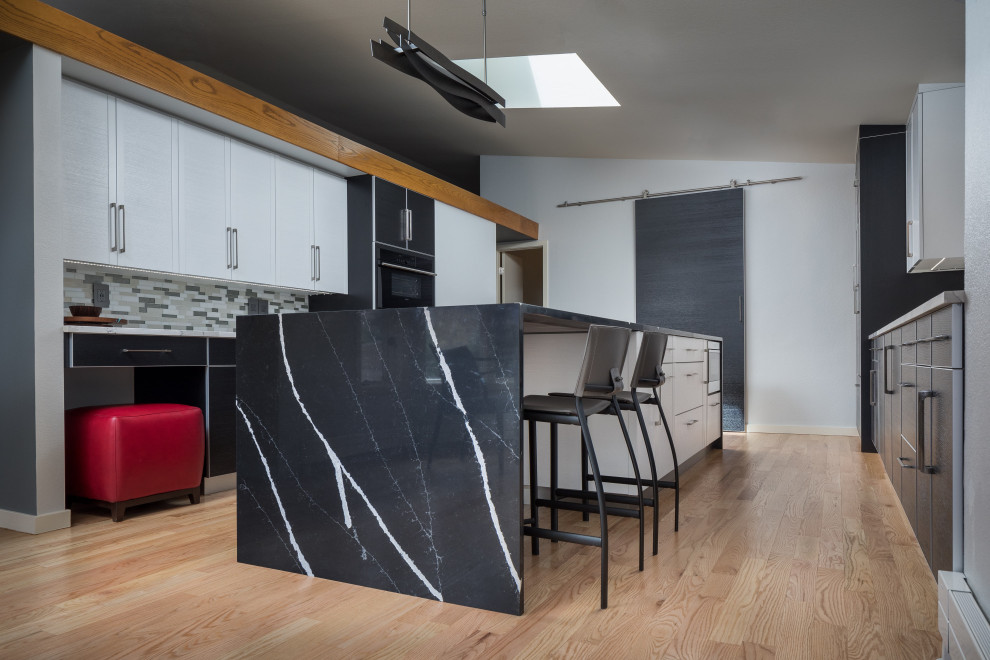 Bild på ett stort funkis svart svart kök, med en köksö, en dubbel diskho, släta luckor, bänkskiva i kvarts, vitt stänkskydd, stänkskydd i glaskakel, integrerade vitvaror, ljust trägolv och brunt golv