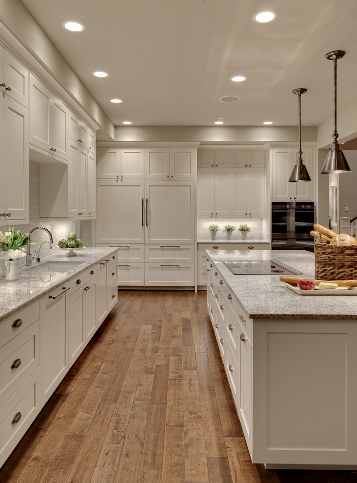 Design ideas for an expansive transitional kitchen in Seattle with an undermount sink, shaker cabinets, white splashback, panelled appliances, granite benchtops, glass tile splashback, medium hardwood floors, with island, white cabinets and grey benchtop.