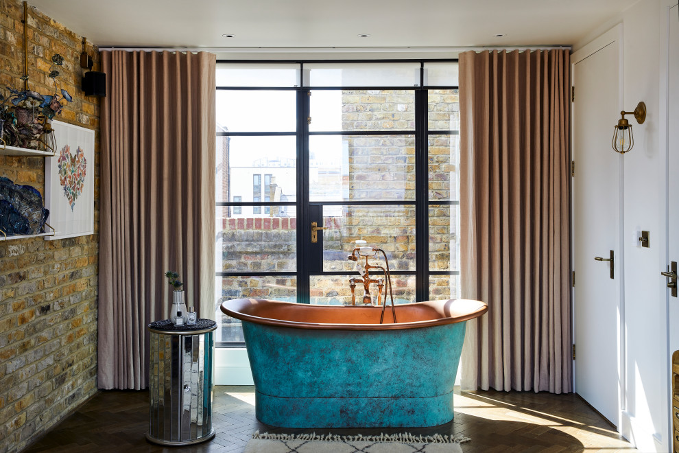 This is an example of a contemporary bathroom in London with a freestanding tub, dark hardwood floors, brown floor and brick walls.