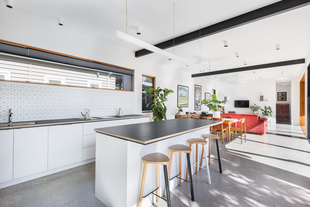 Photo of a contemporary galley kitchen in Melbourne with an undermount sink, flat-panel cabinets, white cabinets, white splashback, mosaic tile splashback, concrete floors, with island, grey floor and black benchtop.