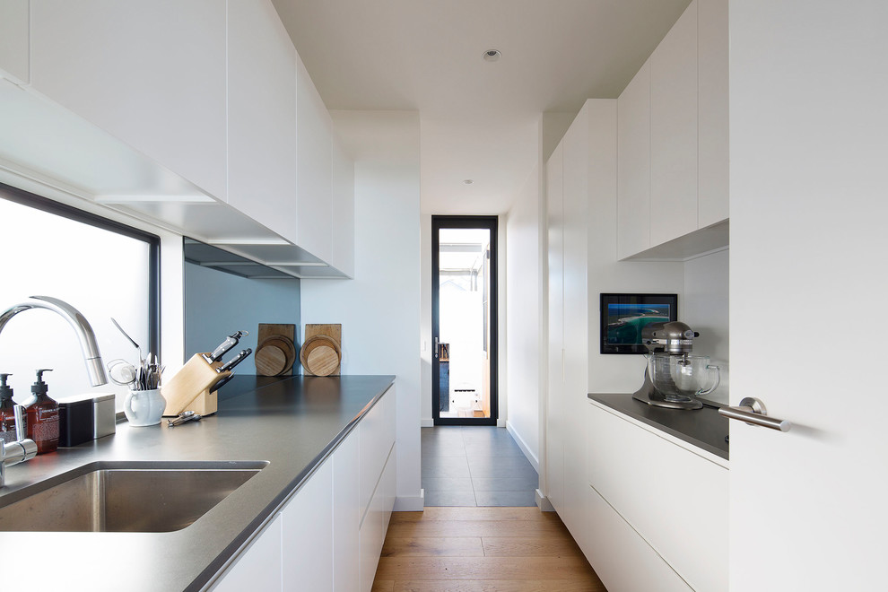 Photo of a large contemporary l-shaped open plan kitchen in Sydney with an undermount sink, flat-panel cabinets, white cabinets, quartz benchtops, metallic splashback, mirror splashback, stainless steel appliances, medium hardwood floors and with island.