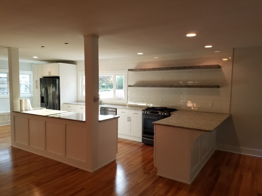 Example of a mid-sized transitional l-shaped medium tone wood floor and brown floor open concept kitchen design with an undermount sink, recessed-panel cabinets, white cabinets, granite countertops, white backsplash, subway tile backsplash, black appliances, an island and beige countertops