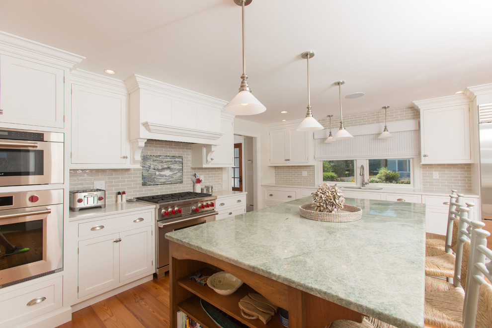Photo of a mid-sized beach style u-shaped eat-in kitchen in Boston with an undermount sink, shaker cabinets, white cabinets, granite benchtops, grey splashback, ceramic splashback, stainless steel appliances, medium hardwood floors, with island and brown floor.