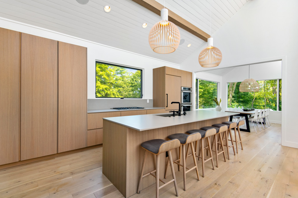 Photo of a contemporary single-wall eat-in kitchen with light wood cabinets, concrete benchtops, grey splashback, stainless steel appliances, light hardwood floors, with island, beige floor and grey benchtop.