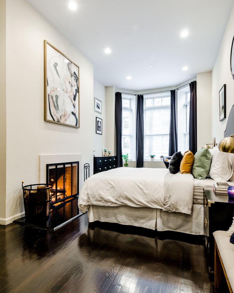 Small eclectic master bedroom in New York with beige walls, dark hardwood floors, a standard fireplace, a stone fireplace surround and brown floor.