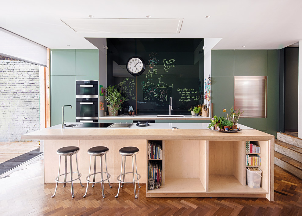 Inspiration for a mid-sized contemporary galley kitchen in Oxfordshire with flat-panel cabinets, green cabinets, dark hardwood floors, with island, brown floor, an undermount sink, black splashback and stainless steel appliances.